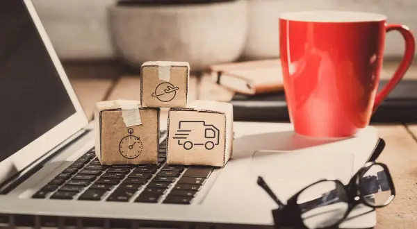 Miniaturki paczek z ikonami transportu na klawiaturze laptopa. Zastanawiasz się, ile zarabia spedytor?